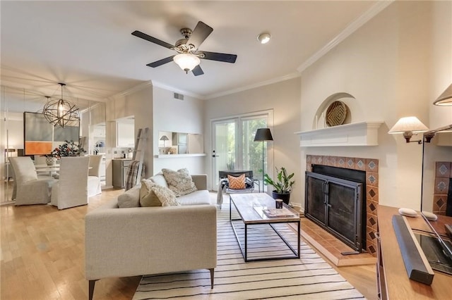 living room with ceiling fan with notable chandelier, light wood-type flooring, crown molding, and a tile fireplace