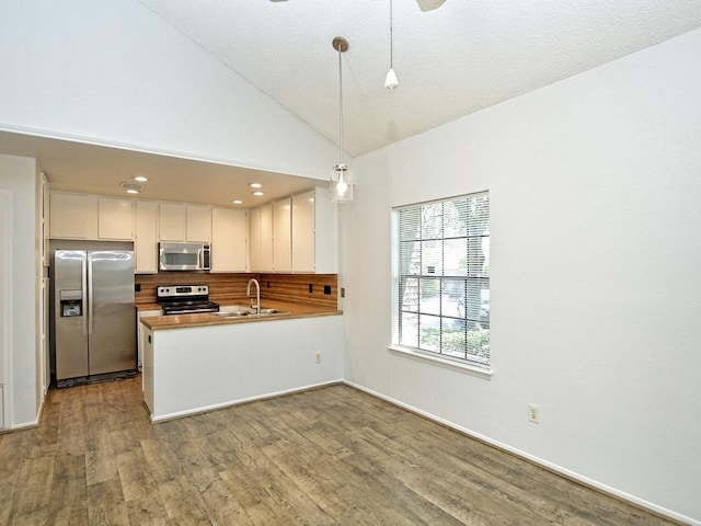 kitchen featuring kitchen peninsula, stainless steel appliances, sink, decorative light fixtures, and white cabinetry