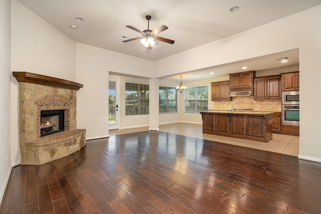 living room with ceiling fan with notable chandelier, hardwood / wood-style flooring, and a stone fireplace