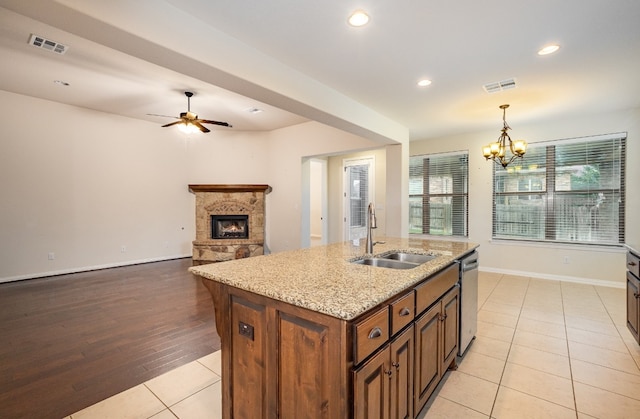 kitchen featuring sink, a kitchen island with sink, light hardwood / wood-style flooring, dishwasher, and a fireplace