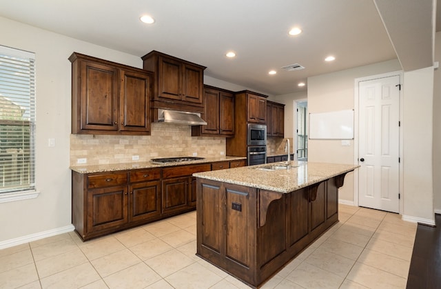 kitchen with ventilation hood, a breakfast bar area, a center island with sink, stainless steel appliances, and light stone countertops