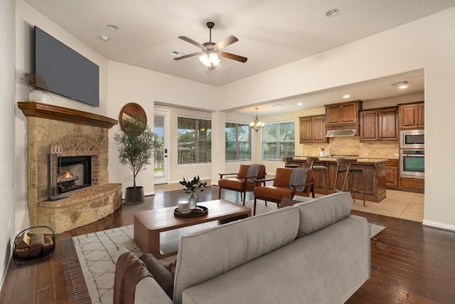 living room with ceiling fan with notable chandelier, a fireplace, hardwood / wood-style floors, and sink