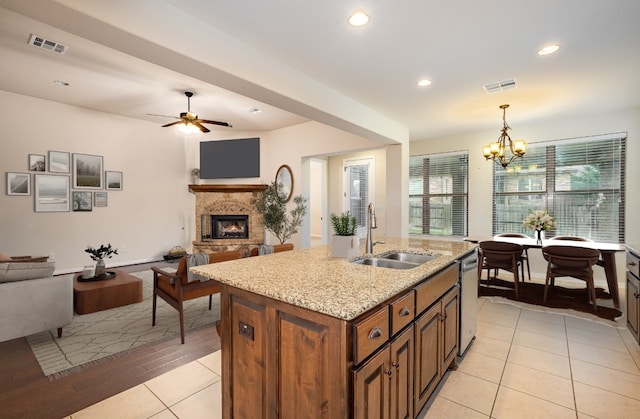 kitchen featuring a kitchen island with sink, light wood-type flooring, pendant lighting, sink, and dishwasher