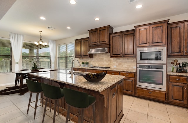 kitchen with an inviting chandelier, sink, an island with sink, appliances with stainless steel finishes, and exhaust hood