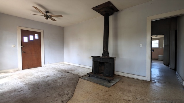 unfurnished living room with ceiling fan, concrete floors, and a wood stove