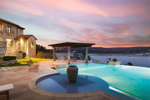 pool at dusk featuring a water view and a patio