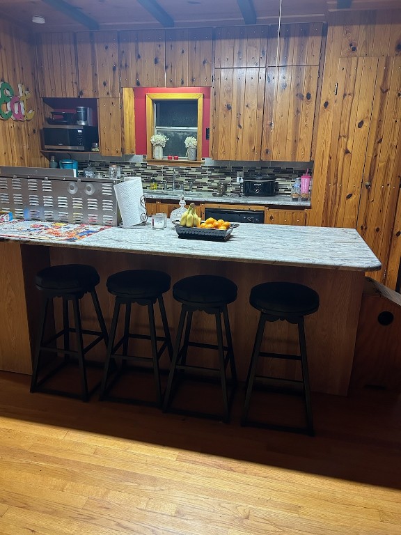 kitchen with a breakfast bar, light hardwood / wood-style flooring, dishwasher, and wooden walls