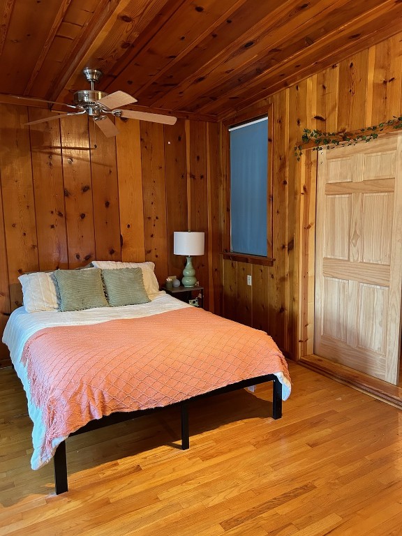 bedroom with wood ceiling, wood walls, ceiling fan, and light hardwood / wood-style floors