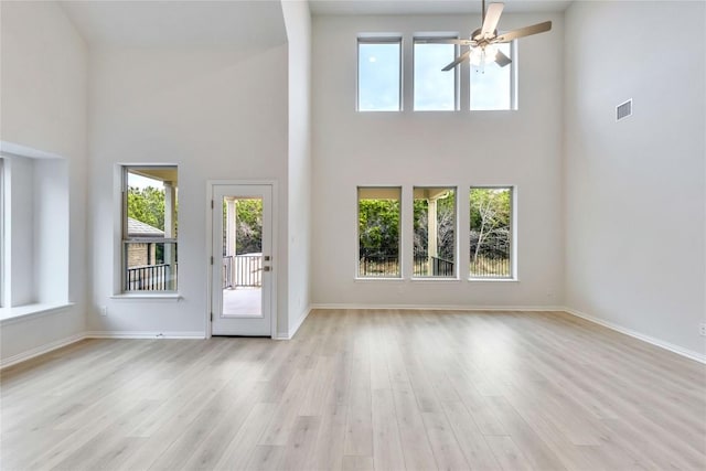 unfurnished living room with a towering ceiling, light hardwood / wood-style flooring, and ceiling fan