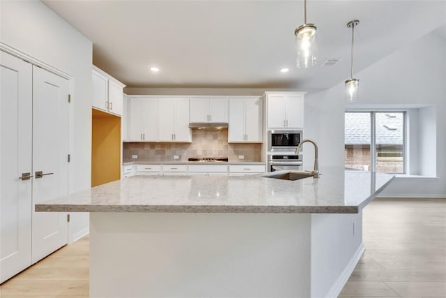 kitchen featuring appliances with stainless steel finishes, decorative light fixtures, light stone counters, and sink