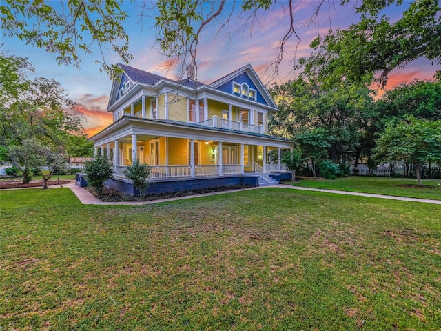 back of property at dusk with covered porch, a lawn, and a balcony