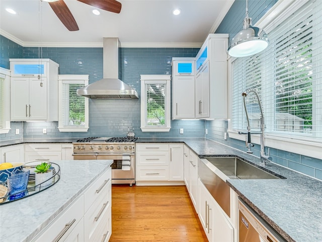 kitchen featuring crown molding, light wood-style floors, wall chimney range hood, appliances with stainless steel finishes, and a sink