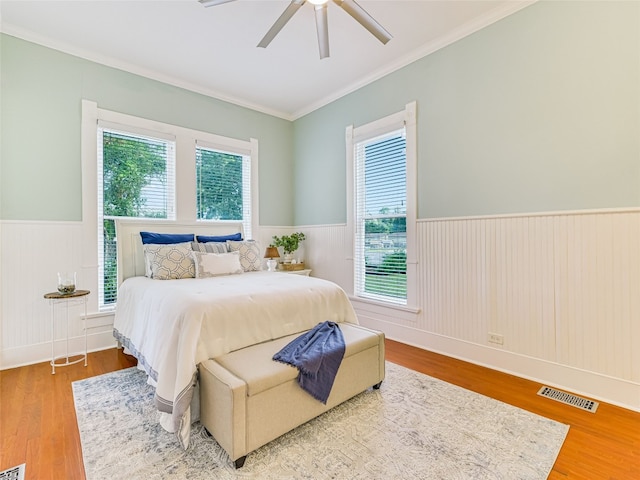 bedroom featuring ceiling fan, ornamental molding, multiple windows, and hardwood / wood-style floors