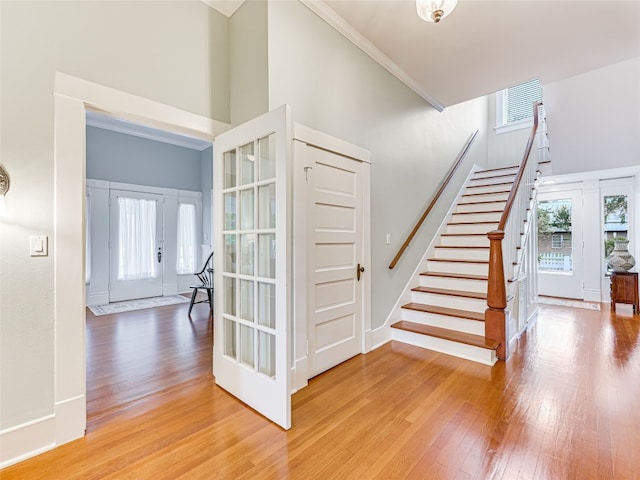 stairway featuring baseboards, wood-type flooring, a high ceiling, and ornamental molding