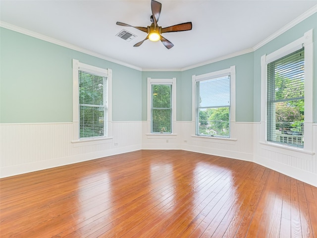 empty room featuring visible vents, a ceiling fan, hardwood / wood-style flooring, crown molding, and a wainscoted wall