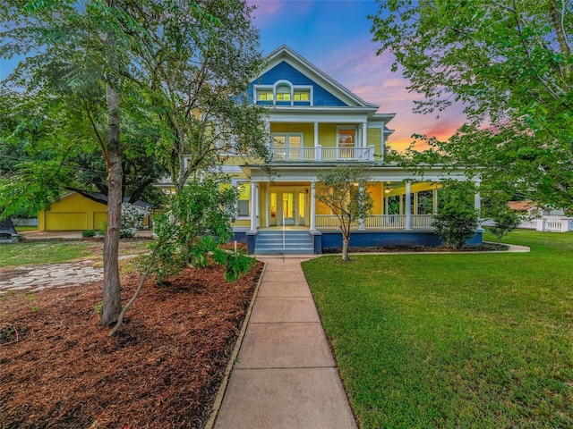 view of front facade with a front yard, french doors, a porch, and a balcony