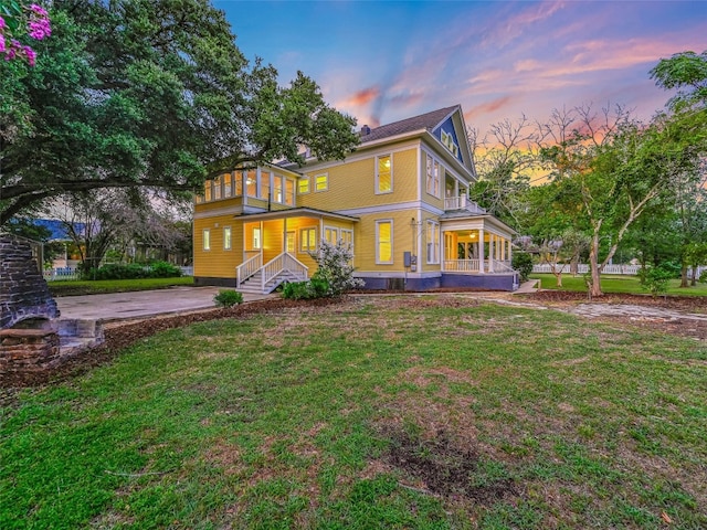 back of house at dusk featuring a yard and a porch