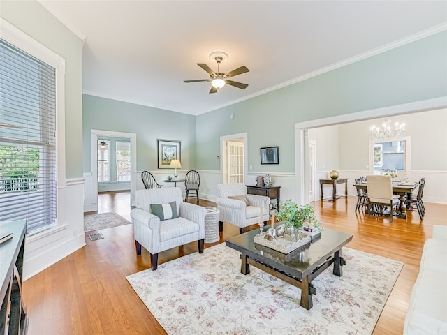 living area featuring light wood-type flooring, ceiling fan with notable chandelier, and a wainscoted wall