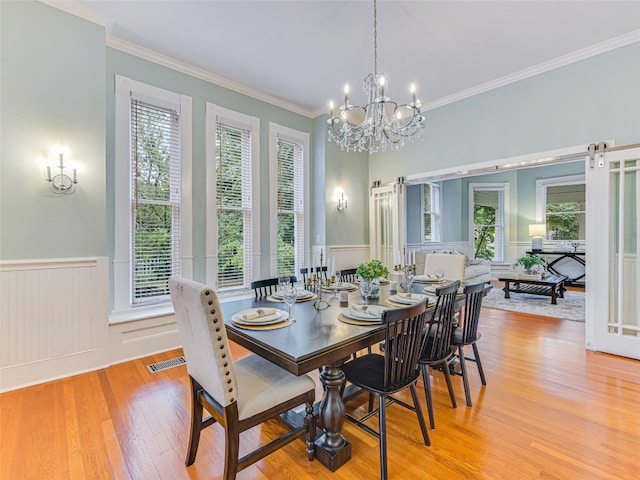 dining room featuring plenty of natural light, light wood finished floors, visible vents, and wainscoting