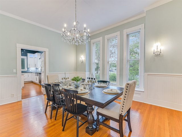 dining area featuring light wood-style floors, ornamental molding, an inviting chandelier, and a wainscoted wall