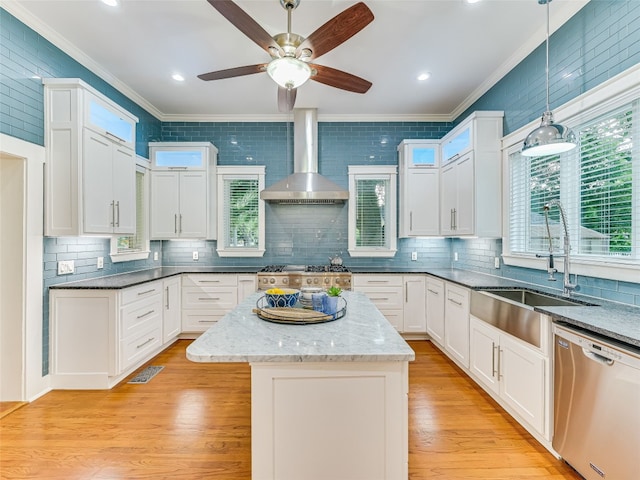 kitchen featuring wall chimney range hood, crown molding, light wood-style floors, dishwasher, and a sink