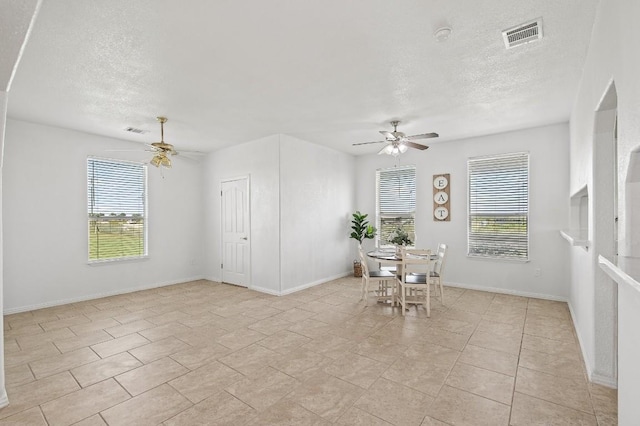 unfurnished dining area featuring light tile patterned floors, a textured ceiling, ceiling fan, and a healthy amount of sunlight