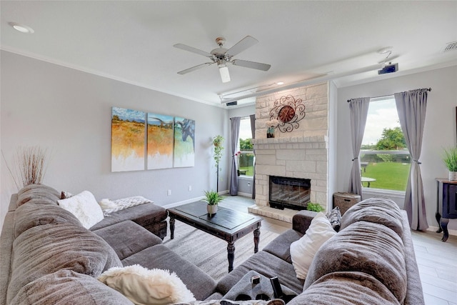 living room with ceiling fan, a stone fireplace, crown molding, and light hardwood / wood-style flooring