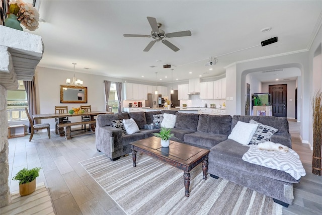 living room with light wood-type flooring, ceiling fan with notable chandelier, and crown molding