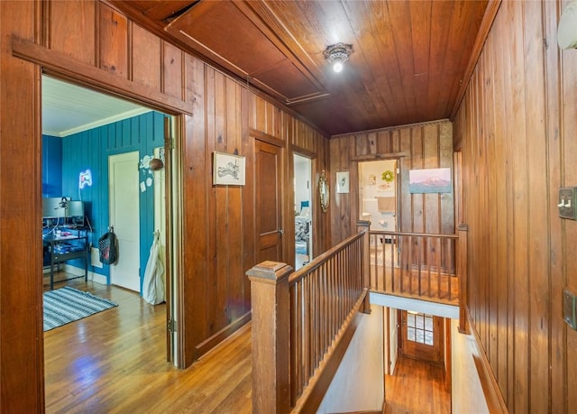 hallway featuring crown molding, wooden ceiling, wood walls, and light wood-type flooring