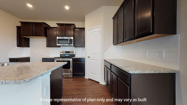 kitchen with appliances with stainless steel finishes, dark hardwood / wood-style floors, light stone counters, dark brown cabinetry, and tasteful backsplash