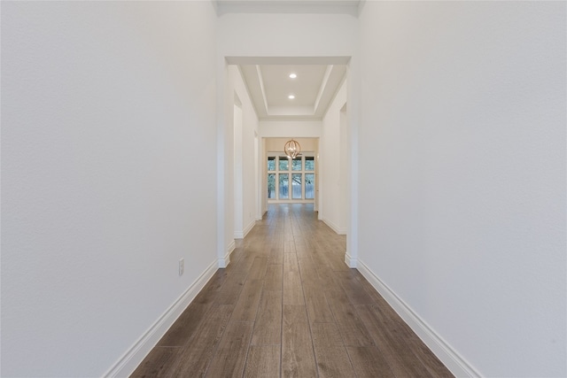 corridor featuring a raised ceiling, dark hardwood / wood-style flooring, and an inviting chandelier