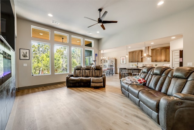 living room with a towering ceiling, ceiling fan with notable chandelier, and light wood-type flooring