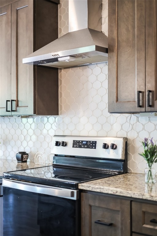 kitchen featuring tasteful backsplash, stainless steel electric range oven, wall chimney range hood, and light stone counters