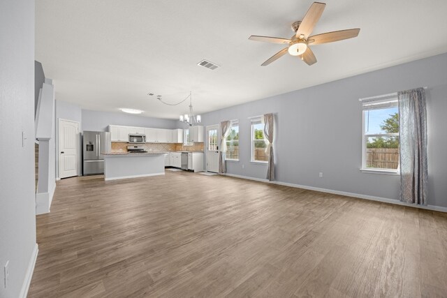 unfurnished living room with ceiling fan with notable chandelier and hardwood / wood-style flooring