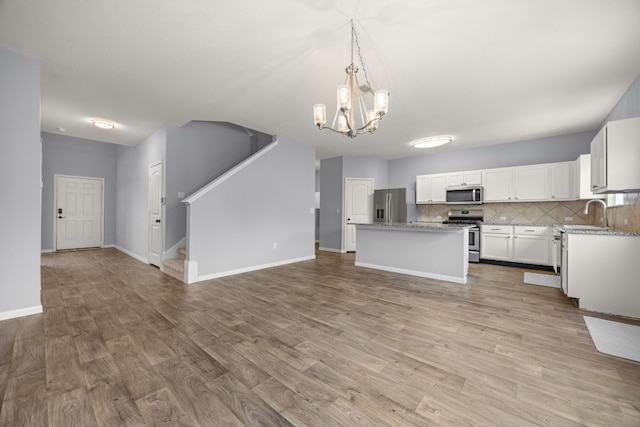 kitchen with stainless steel appliances, white cabinetry, a kitchen island, pendant lighting, and a notable chandelier