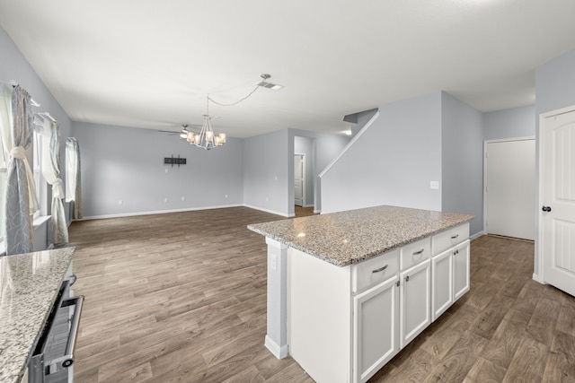 kitchen with light stone countertops, light hardwood / wood-style flooring, a center island, decorative light fixtures, and white cabinetry