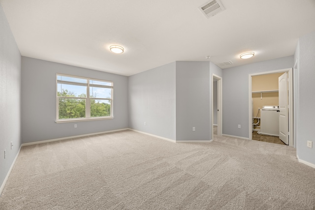 unfurnished bedroom featuring washer / clothes dryer, a closet, a spacious closet, and light carpet