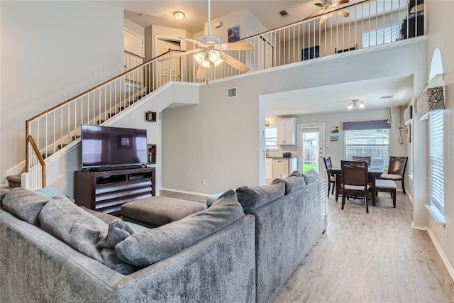 living room featuring ceiling fan, a towering ceiling, and light hardwood / wood-style floors