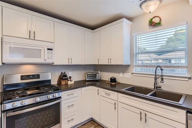 kitchen featuring stainless steel gas range oven, white cabinetry, and sink