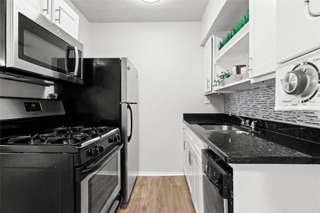 kitchen with appliances with stainless steel finishes, a textured ceiling, sink, light hardwood / wood-style flooring, and white cabinetry