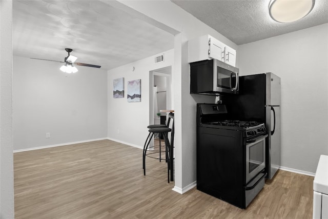 kitchen with white cabinets, ceiling fan, black gas range oven, a textured ceiling, and light hardwood / wood-style floors