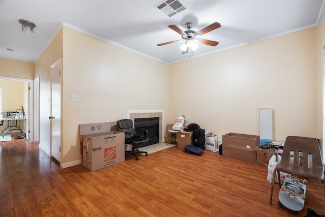 miscellaneous room featuring ceiling fan, a tiled fireplace, crown molding, and hardwood / wood-style flooring