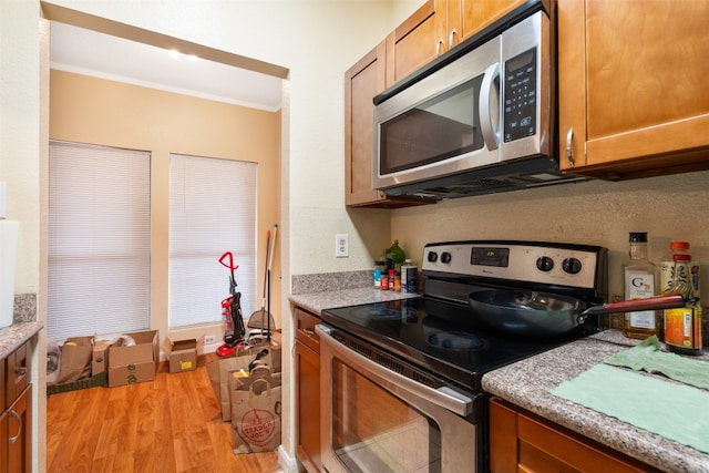 kitchen with ornamental molding, light wood-type flooring, and stainless steel appliances