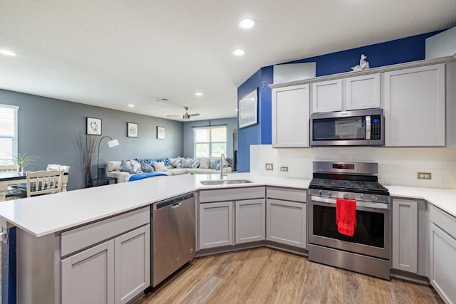 kitchen with kitchen peninsula, appliances with stainless steel finishes, light hardwood / wood-style floors, and sink