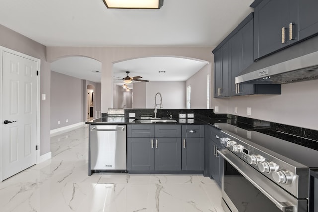 kitchen featuring appliances with stainless steel finishes, exhaust hood, dark stone countertops, sink, and ceiling fan