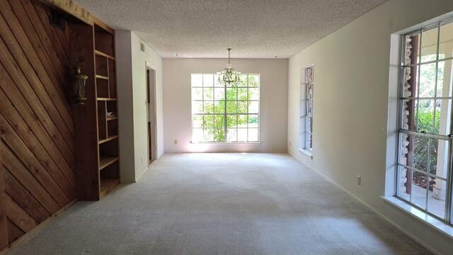 carpeted empty room featuring a textured ceiling and a notable chandelier