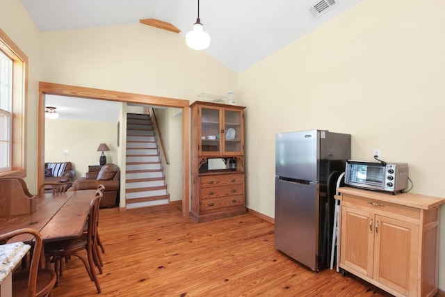 kitchen with high vaulted ceiling, decorative light fixtures, stainless steel fridge, and light wood-type flooring