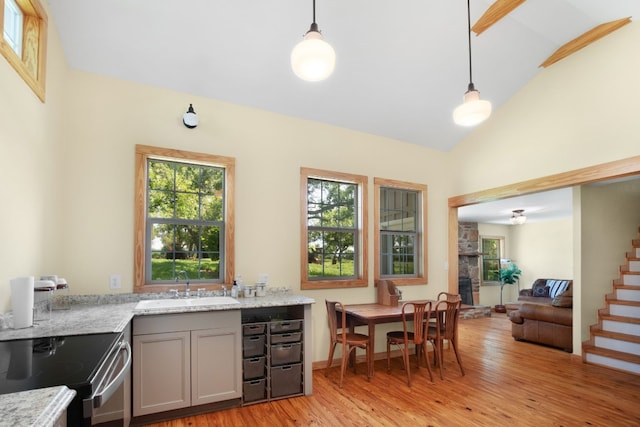 kitchen featuring light wood finished floors, gray cabinetry, decorative light fixtures, light stone counters, and a sink