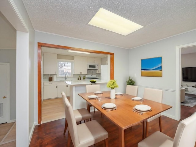 dining room with a textured ceiling, dark hardwood / wood-style floors, crown molding, and sink