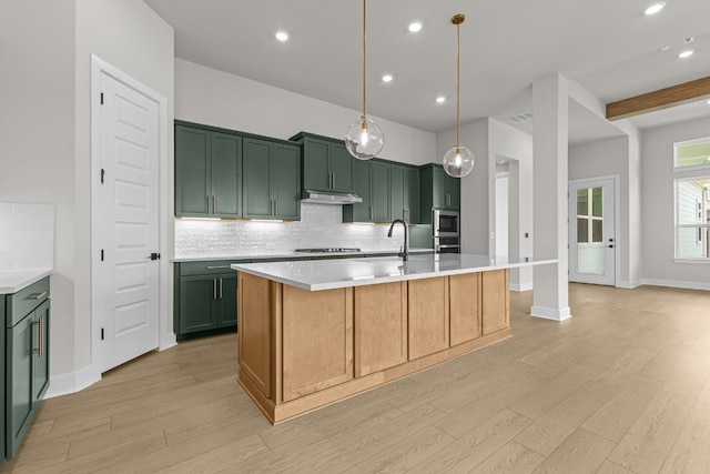 kitchen with decorative light fixtures, gas cooktop, decorative backsplash, light hardwood / wood-style floors, and a kitchen island with sink